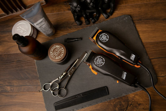Two hair clippers, scissors, a comb, and grooming products on a slate board