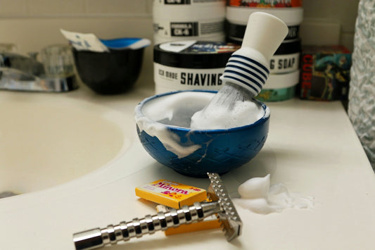 Shaving brush and bowl with lather and razor on sink